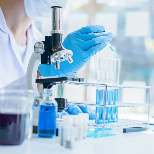 Person in a lab coat using a microscope with test tubes and blue liquid in the background. hydroxyl ionization, pet-safe cleaning technology, science-based pet hygiene, non-toxic pet cleaner
